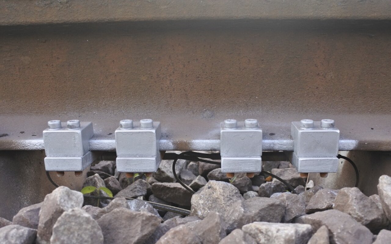 Quatre capteurs encapsulés fixés par brides sur un rail ferroviaire